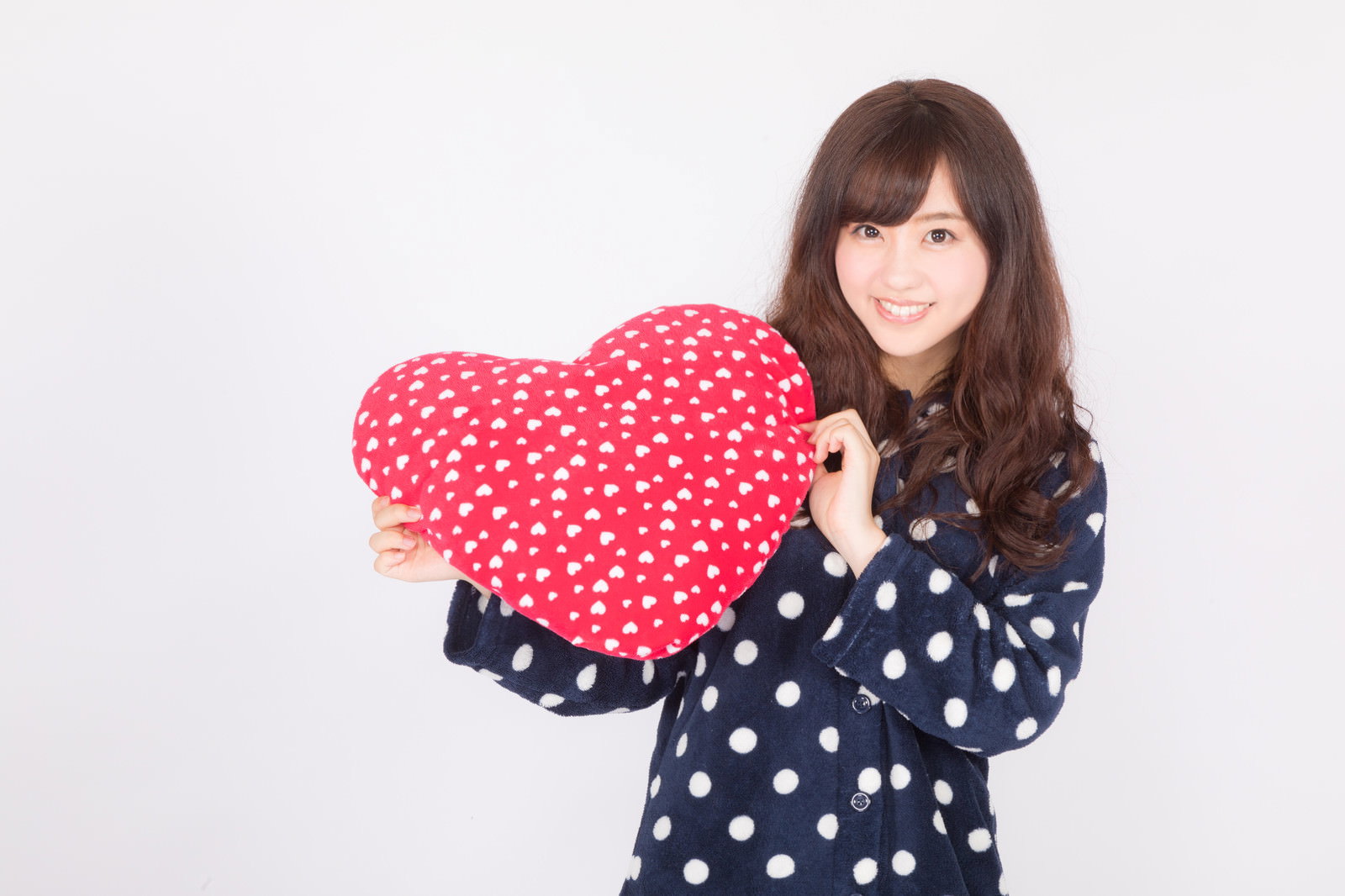 赤いハート型のクッションを胸に抱く水玉パジャマ姿の女性［モデル：河村友歌］