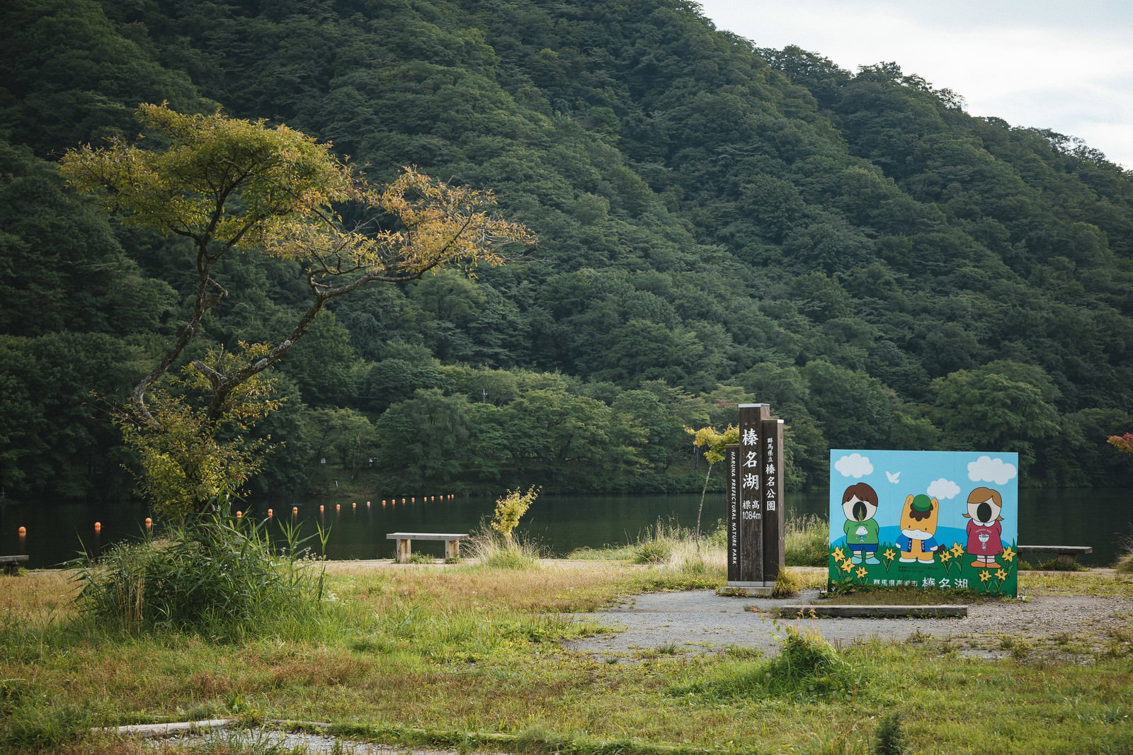 緑の山々を背景に榛名湖と榛名公園の青い看板が立つ風景