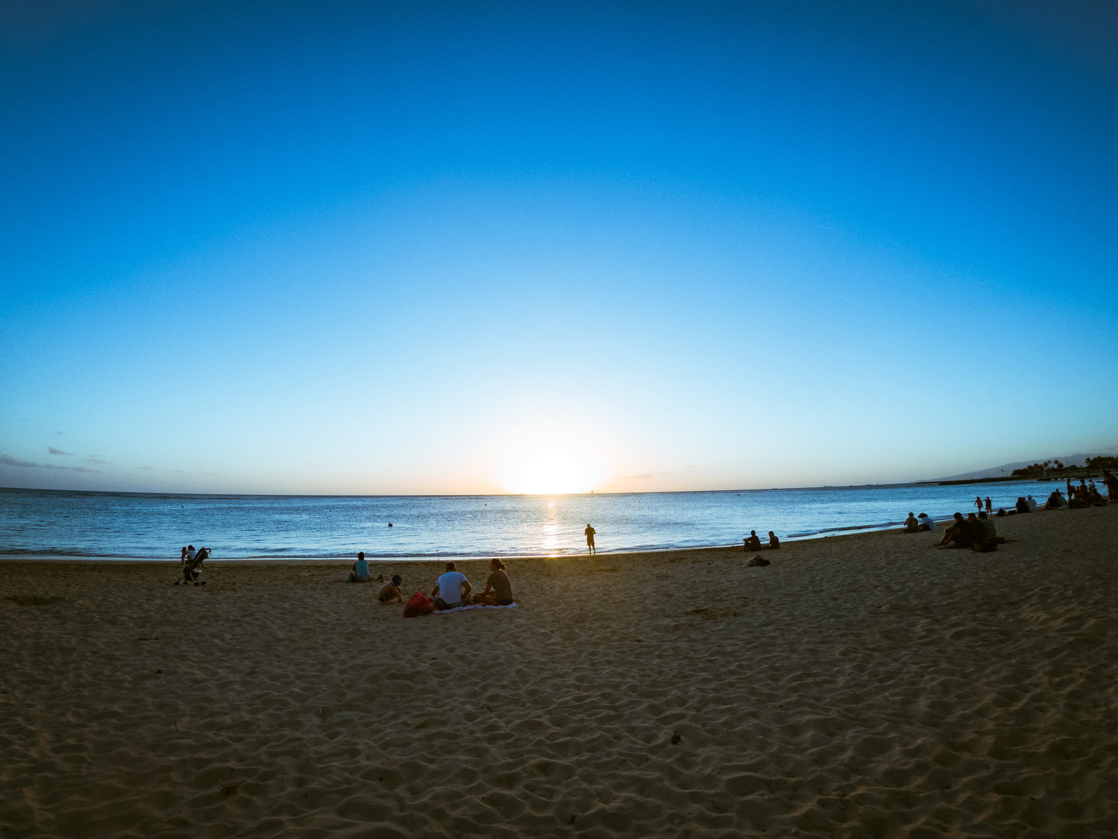 ハワイの砂浜で夕日を眺める人々のシルエット