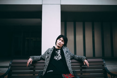 ベンチで悪態をつく黒いジャケットの男性の強面な表情