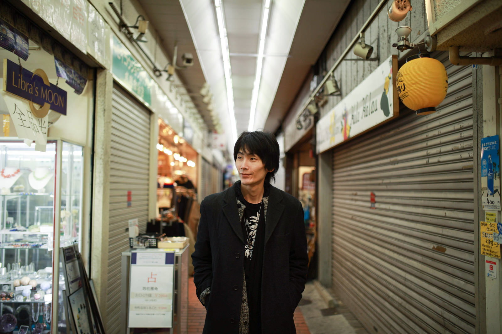 シャッターが閉まった商店街を黒い服装で歩く男性［モデル：ハヤト］