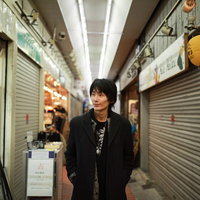 シャッターが閉まった商店街を歩く黒い服装の男性の写真