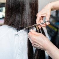 ヘアドネーション用の長い黒髪をハサミでカットする美容師の手元の写真