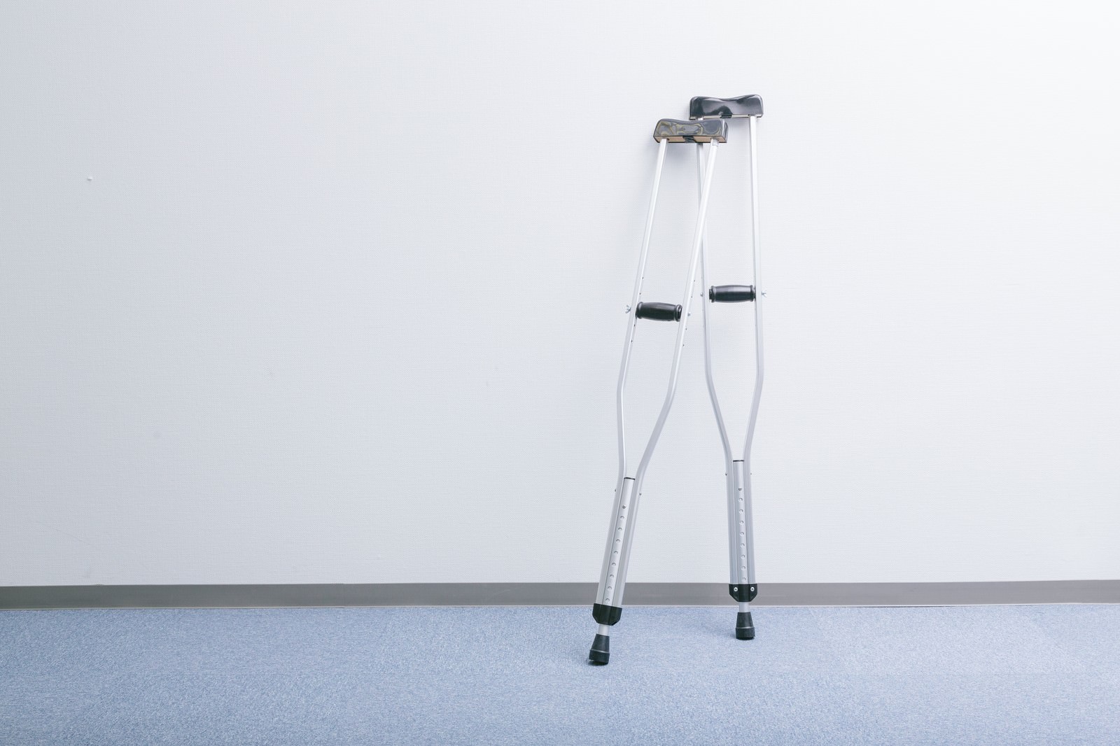 白い壁と床の廊下に立てかけられた2本の銀色の松葉杖
