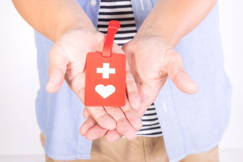 赤いヘルプマークを両手で大切に持って差し出す所持者