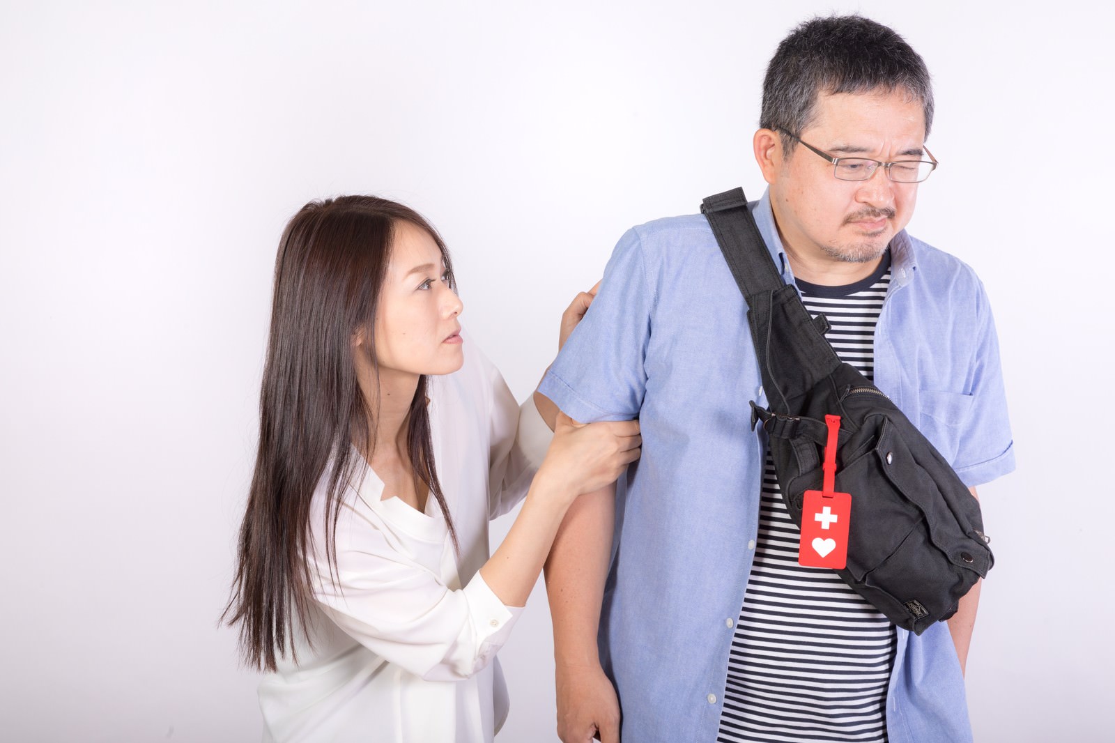 白い背景でヘルプマーク所持者の男性に優しく声をかける女性［モデル：土本寛子 ナリシゲ］