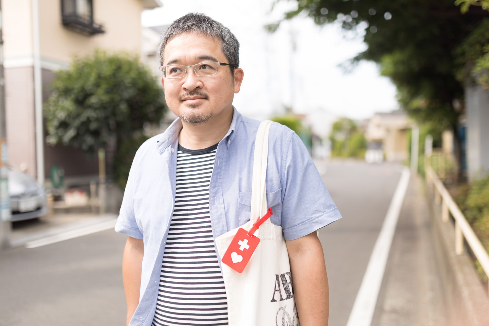 白いトートバッグにヘルプマークをつけてボーダーシャツで歩く男性［モデル：ナリシゲ］