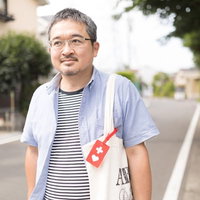 トートバッグに赤いヘルプマークをつけて近所を歩く男性の写真