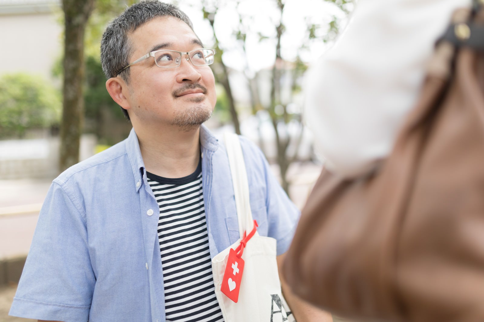 席を譲ってもらい笑顔を見せるヘルプマークを持つ男性［モデル：ナリシゲ］