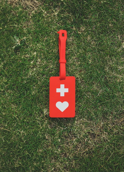 緑の芝生に置かれた赤いヘルプマーク、白い十字とハート