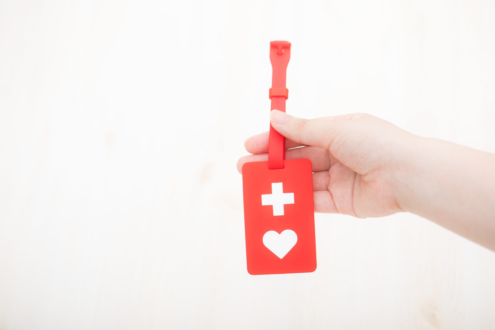 白い背景で赤いヘルプマークを手のひらに持っている様子