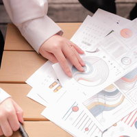 テーブルに広げたグラフや図表が書かれた資料を指で確認の写真