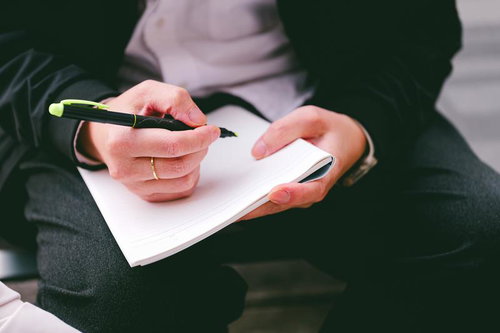 メモ帳に黒いペンで書き込む女性の手元の写真