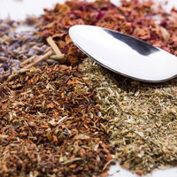 乾燥ハーブ類とスプーン、白いスプーンと茶色や緑色のハーブの写真
