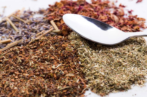 乾燥ハーブ類とスプーン、白いスプーンと茶色や緑色のハーブ