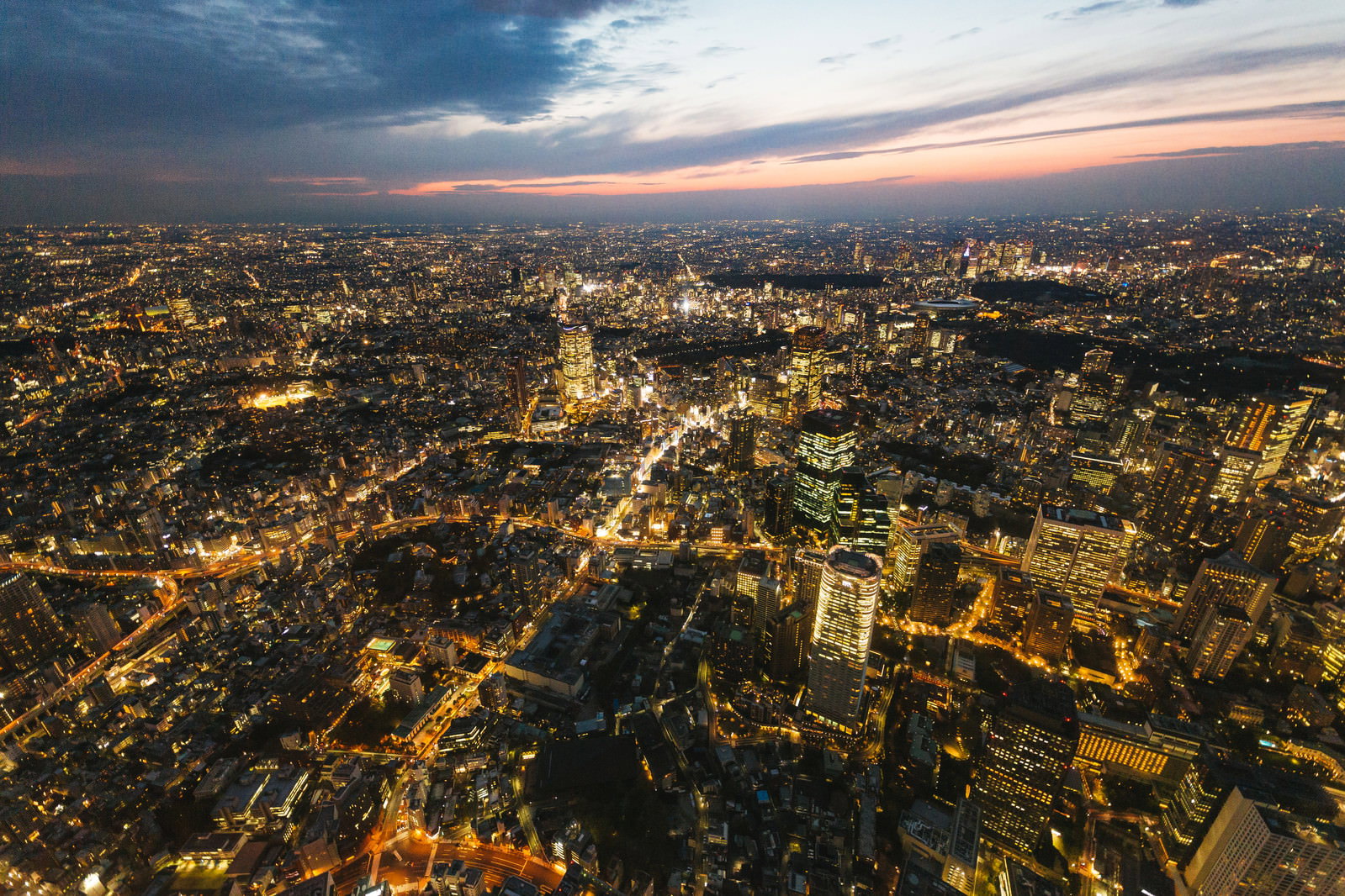 夕暮れ時の東京都心を空撮した夜景、高層ビル群がライトアップされている