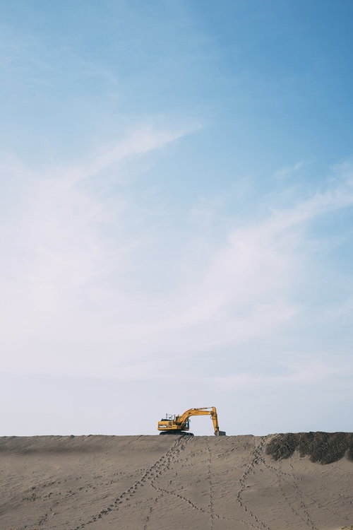 砂地に置かれたオレンジ色のシャベルカーと青空