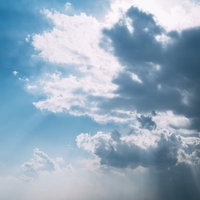 厚い雲の合間から光が差し込む夕方の海と水平線の写真