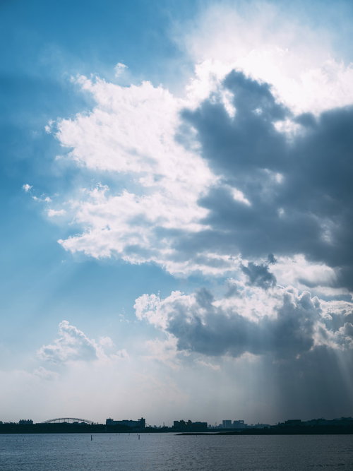 厚い雲の合間から光が差し込む夕方の海と水平線