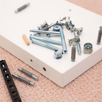 組み立て家具のネジと金具部品、白い板の上に散らばった工具の写真