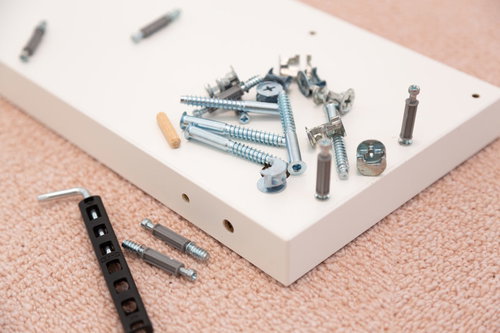 組み立て家具のネジと金具部品、白い板の上に散らばった工具