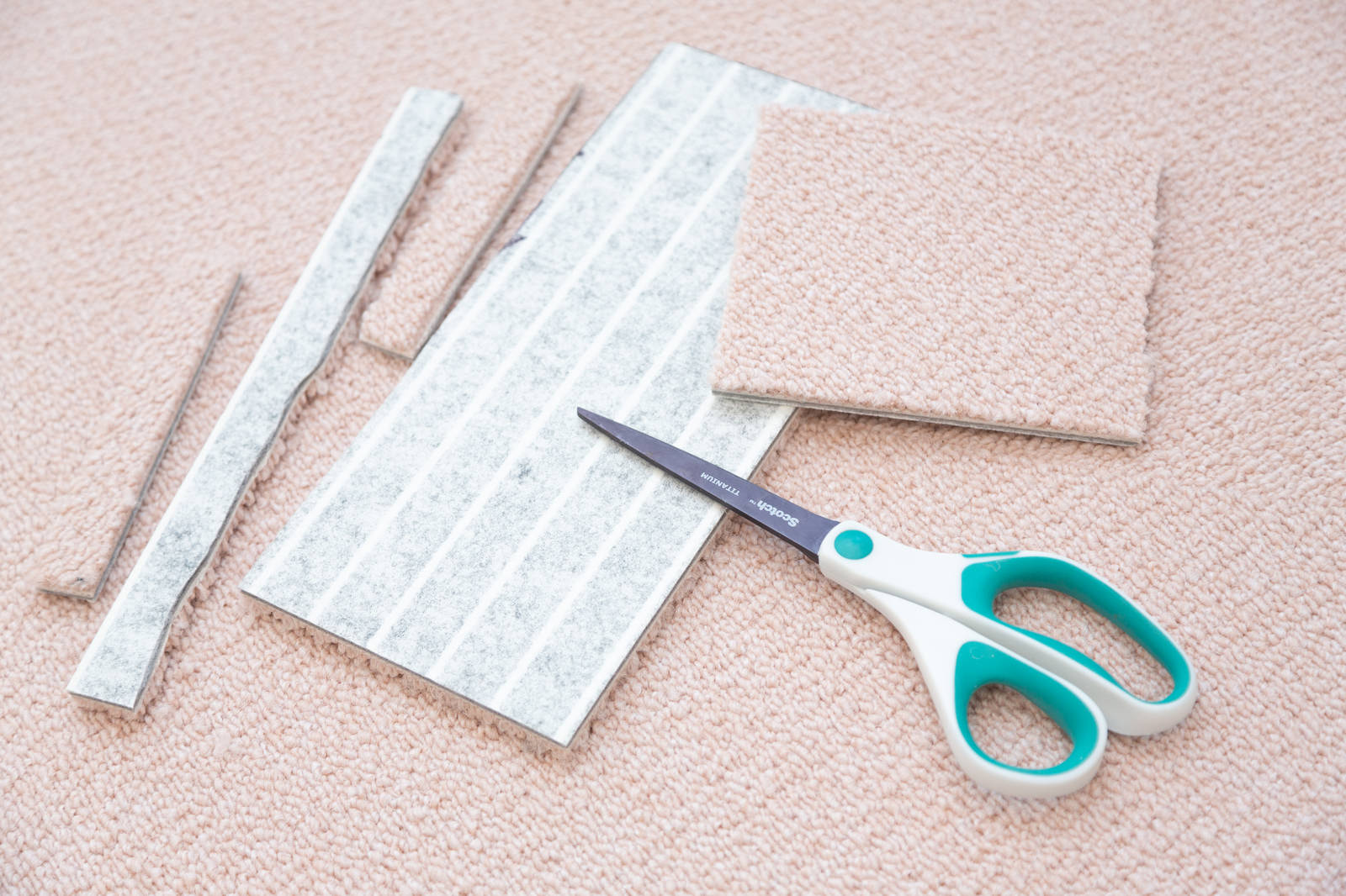 白とベージュ色のタイルカーペットがカットされ、緑色の柄付きはさみが置かれた状態