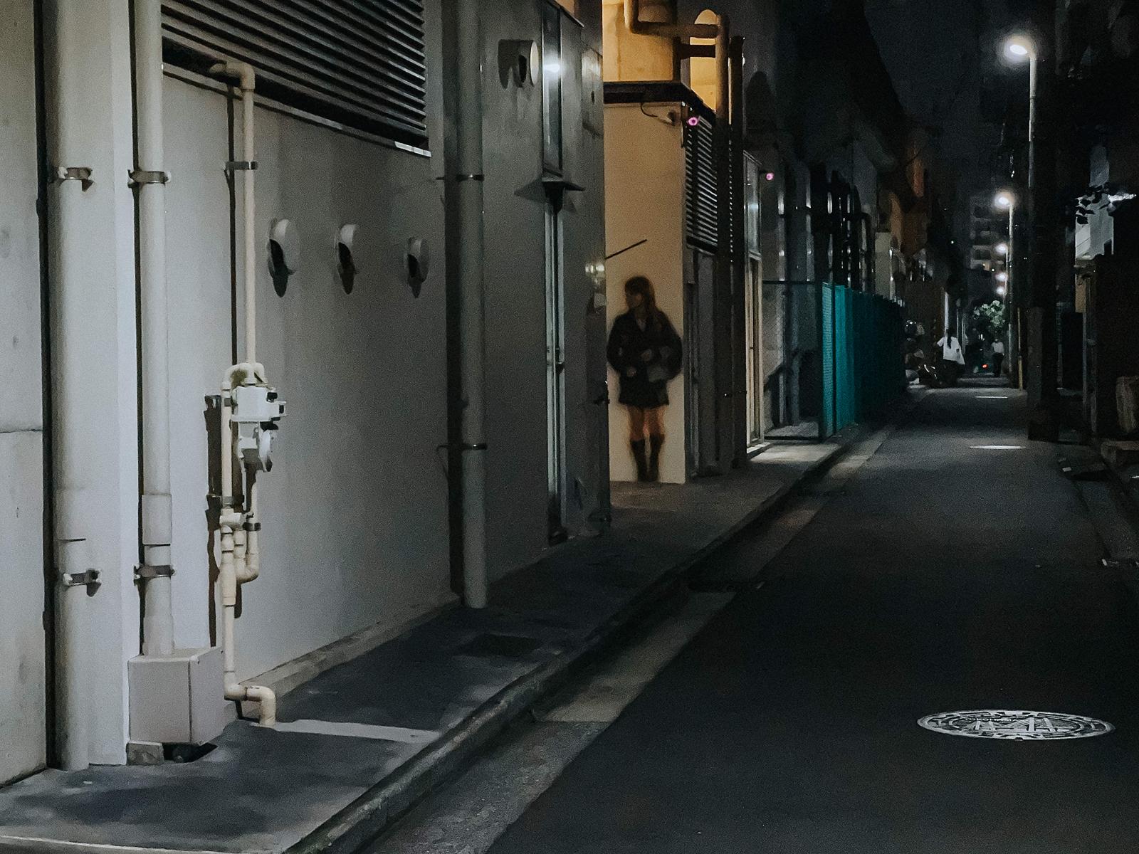 夜間に照らされた路地裏の白い壁に描かれた黒い衣装の女子高生の壁画