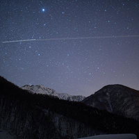 冬の山岳地帯に流れ落ちる星座と流星の輝きの写真