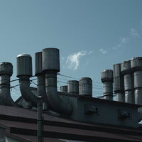 工場の複数の煙突と排気口から排出される排気の写真