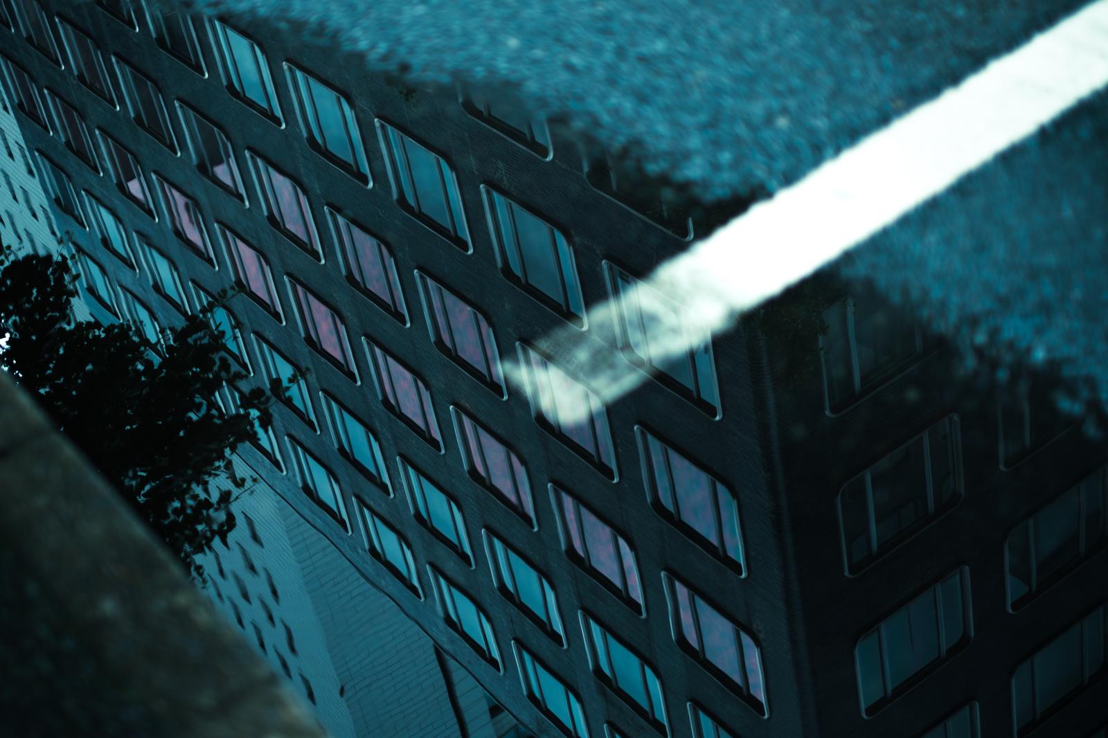 A cityscape of multiple buildings reflected in rain puddles on the street