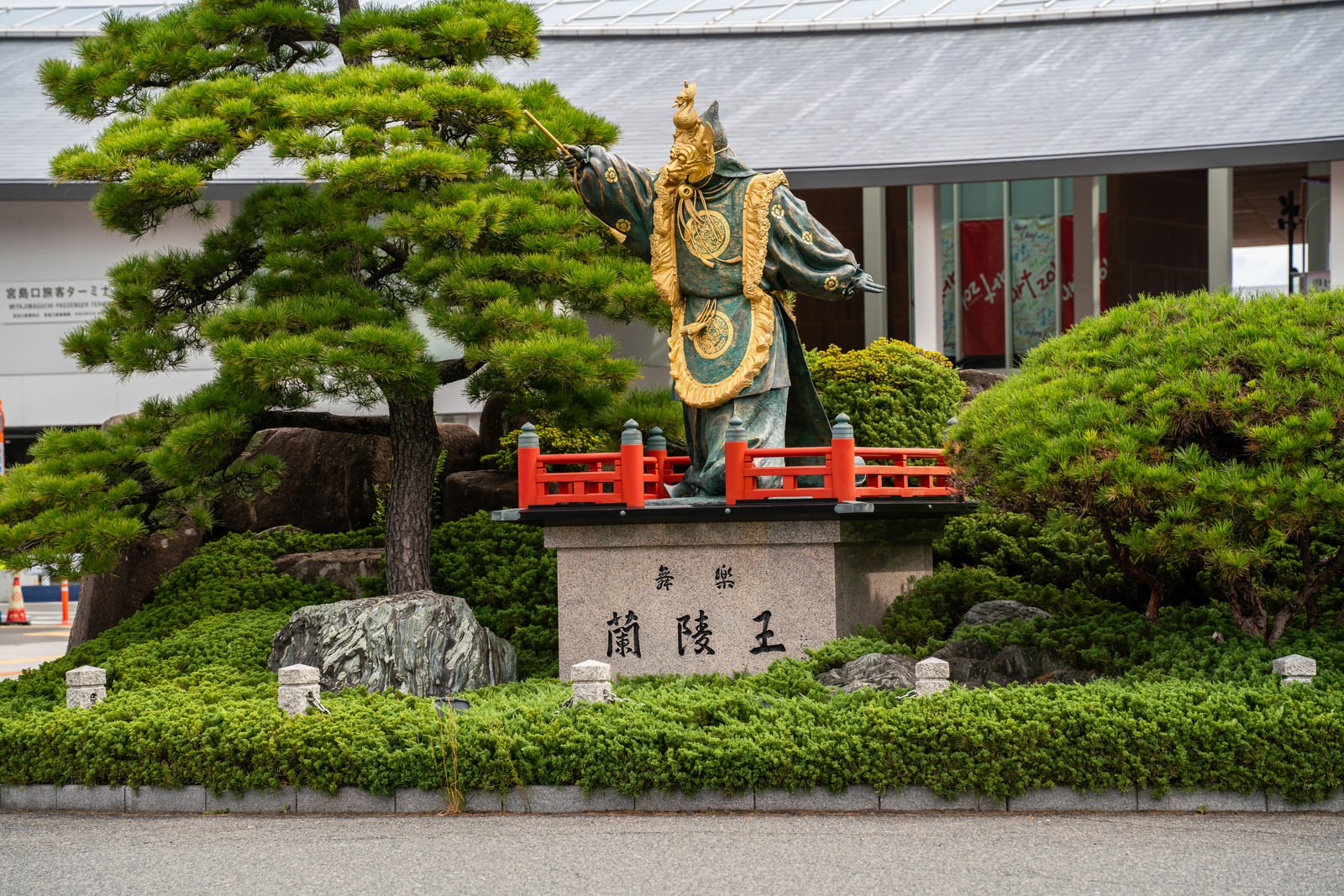 緑の庭園に設置された蘭陵王の銅像と日本建築の建物