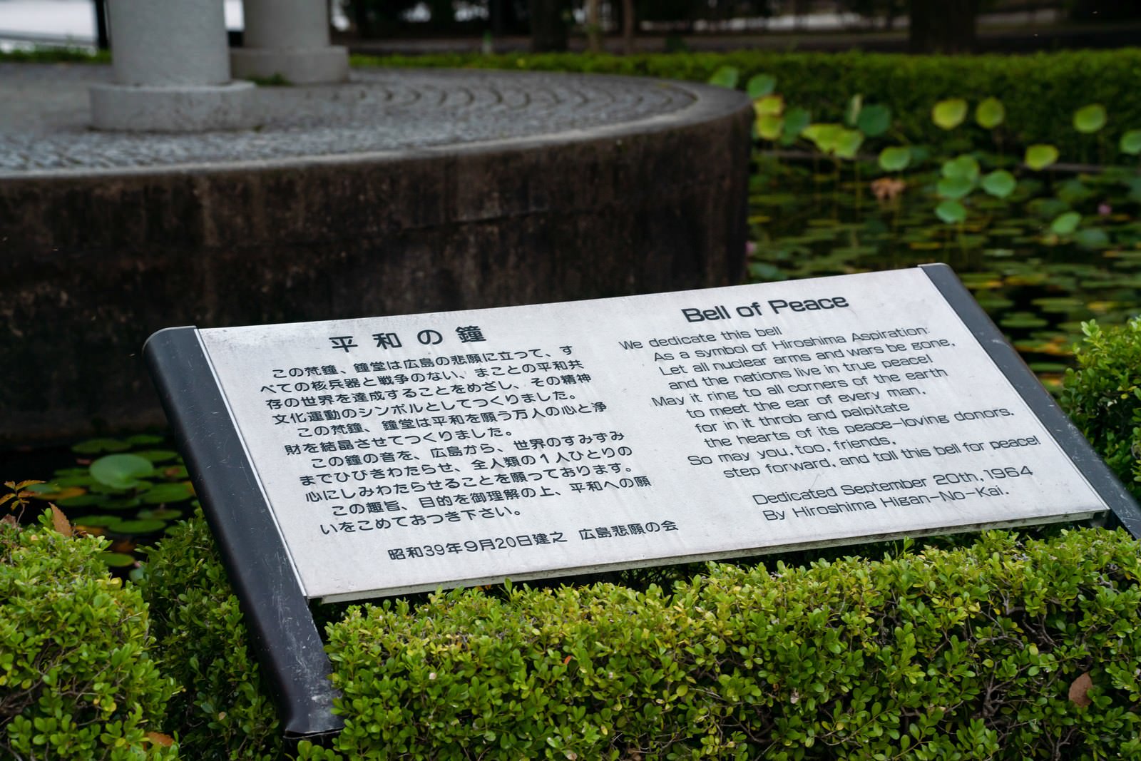 「平和の鐘」と英文で記載された説明プレートが緑の苔むした石に設置されている