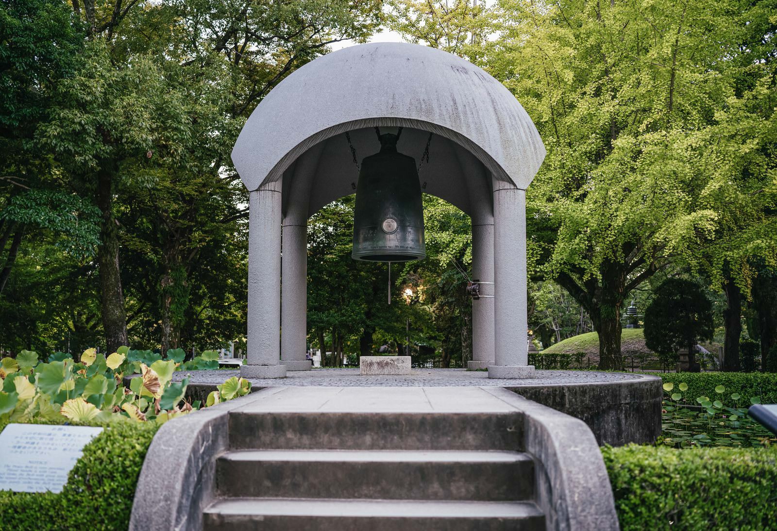 白いドーム屋根の鐘楼に吊られた大きな梵鐘を、木々に囲まれた公園から眺めた風景