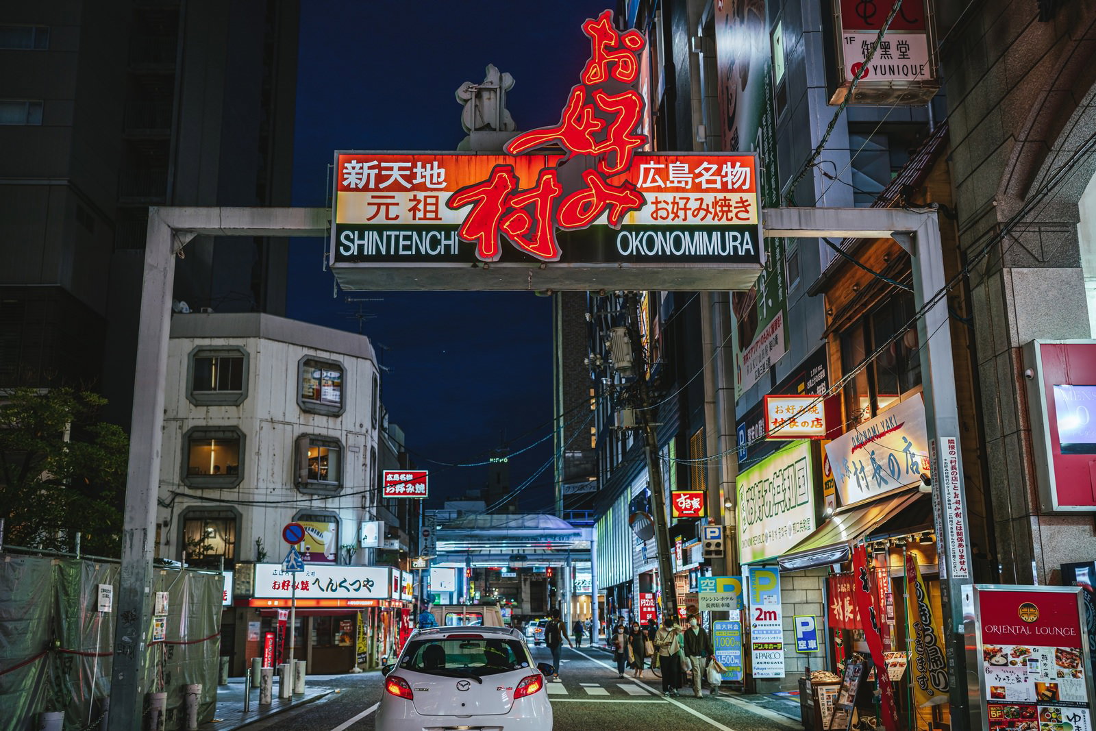 夜間に光る赤いネオン看板のお好み焼き村・新天地の入口と繁華街の風景