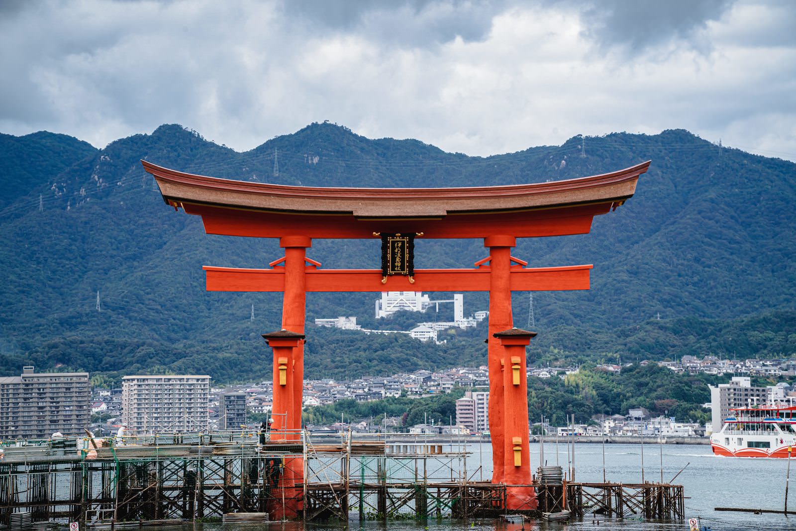 海に立つ厳島神社の朱色の大鳥居と背景の山並み、街並み