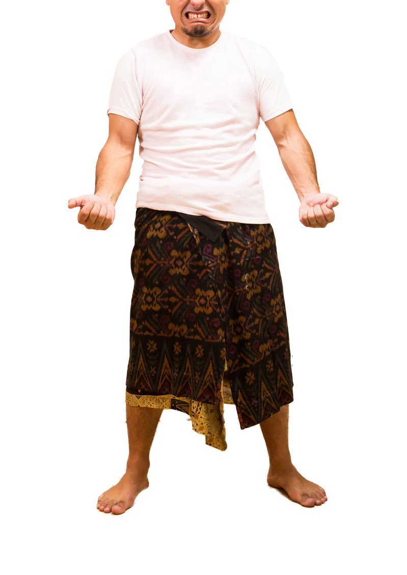 Man in white t-shirt and traditional skirt, arms crossed, with a determined expression