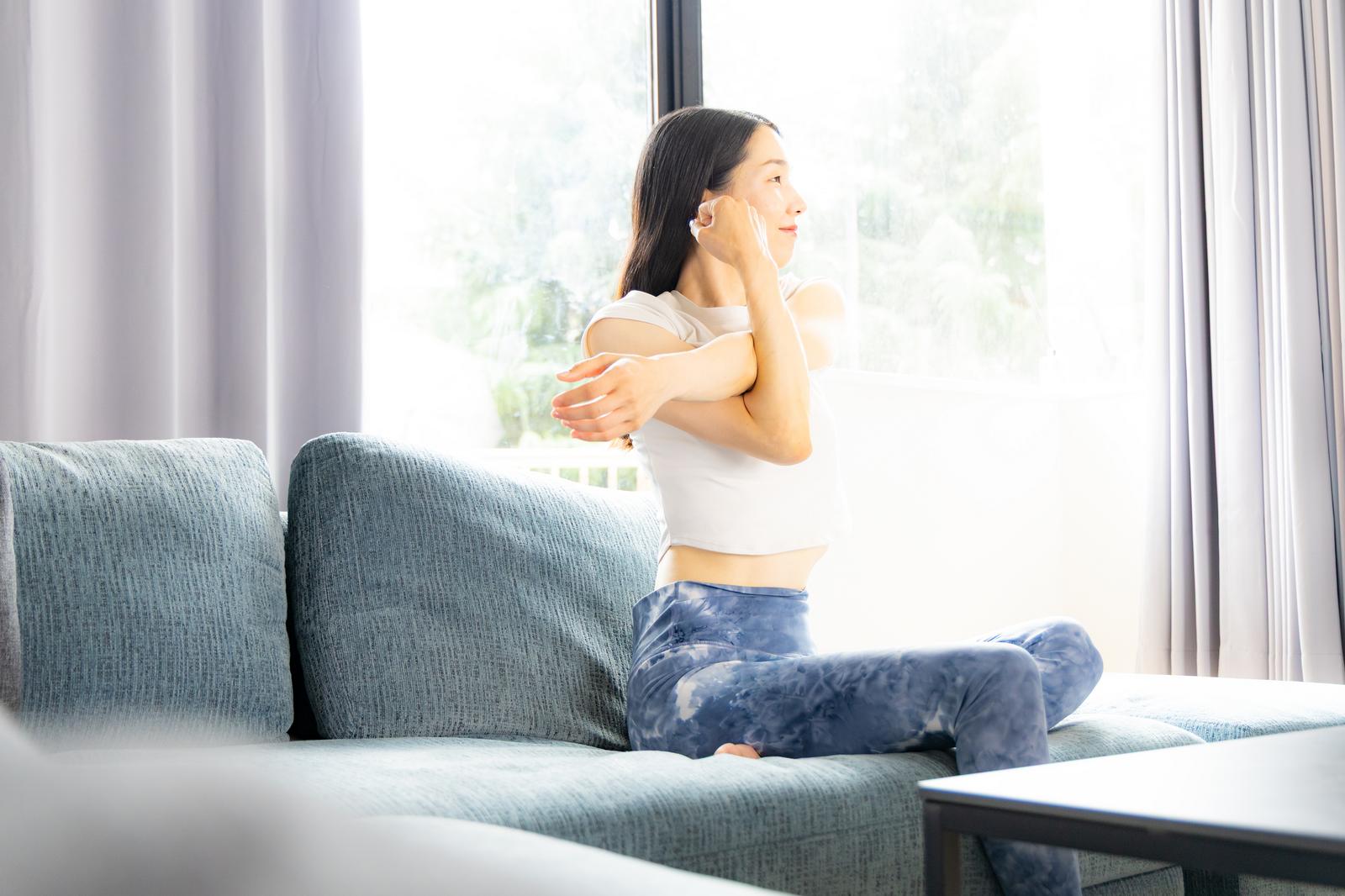Woman in white top doing stretch exercises on living room sofa