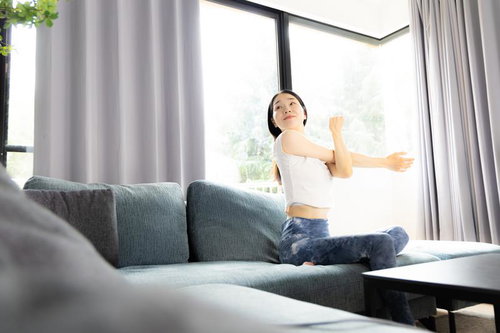 大きな窓のあるリビングでソファーの上でストレッチする女性
