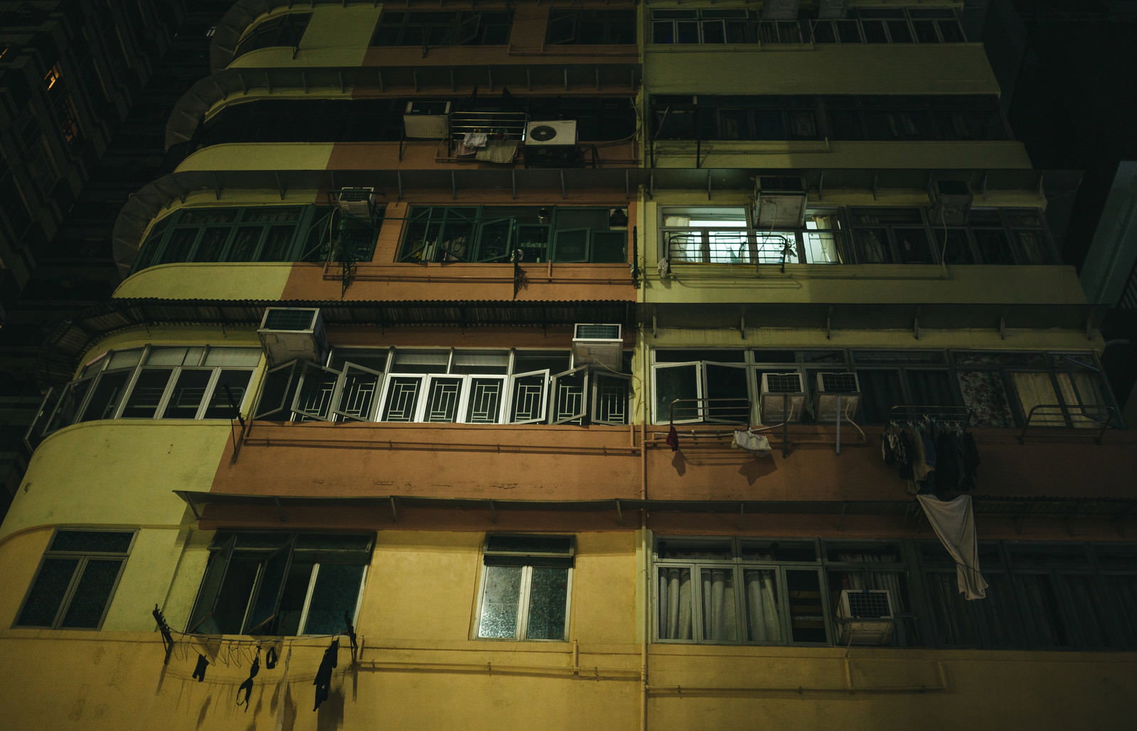 夜間の香港の集合住宅、黄色い照明が窓から漏れ洗濯物が干されている
