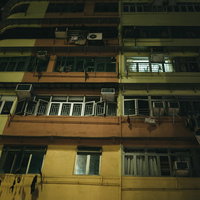 香港の雑居集合住宅、窓から漏れる黄色い照明と洗濯物の写真
