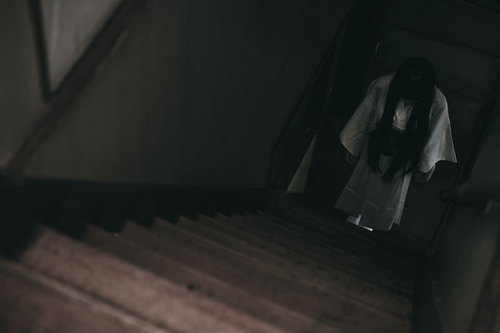 暗い階段下に白装束でうつむき佇む女性のホラー