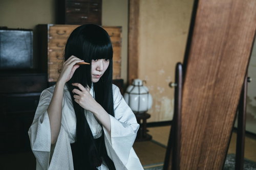 和室の鏡の前で櫛を使って髪をとかす黒髪の女性