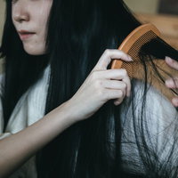 和室で絡まった黒髪を木製の櫛で無理やりとおす女性の写真