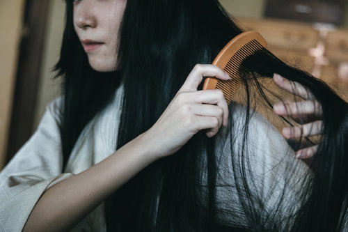 和室で絡まった黒髪を木製の櫛で無理やりとおす女性