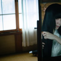 鏡を見ながら長い黒髪を櫛でとかす女性の後ろ姿の写真