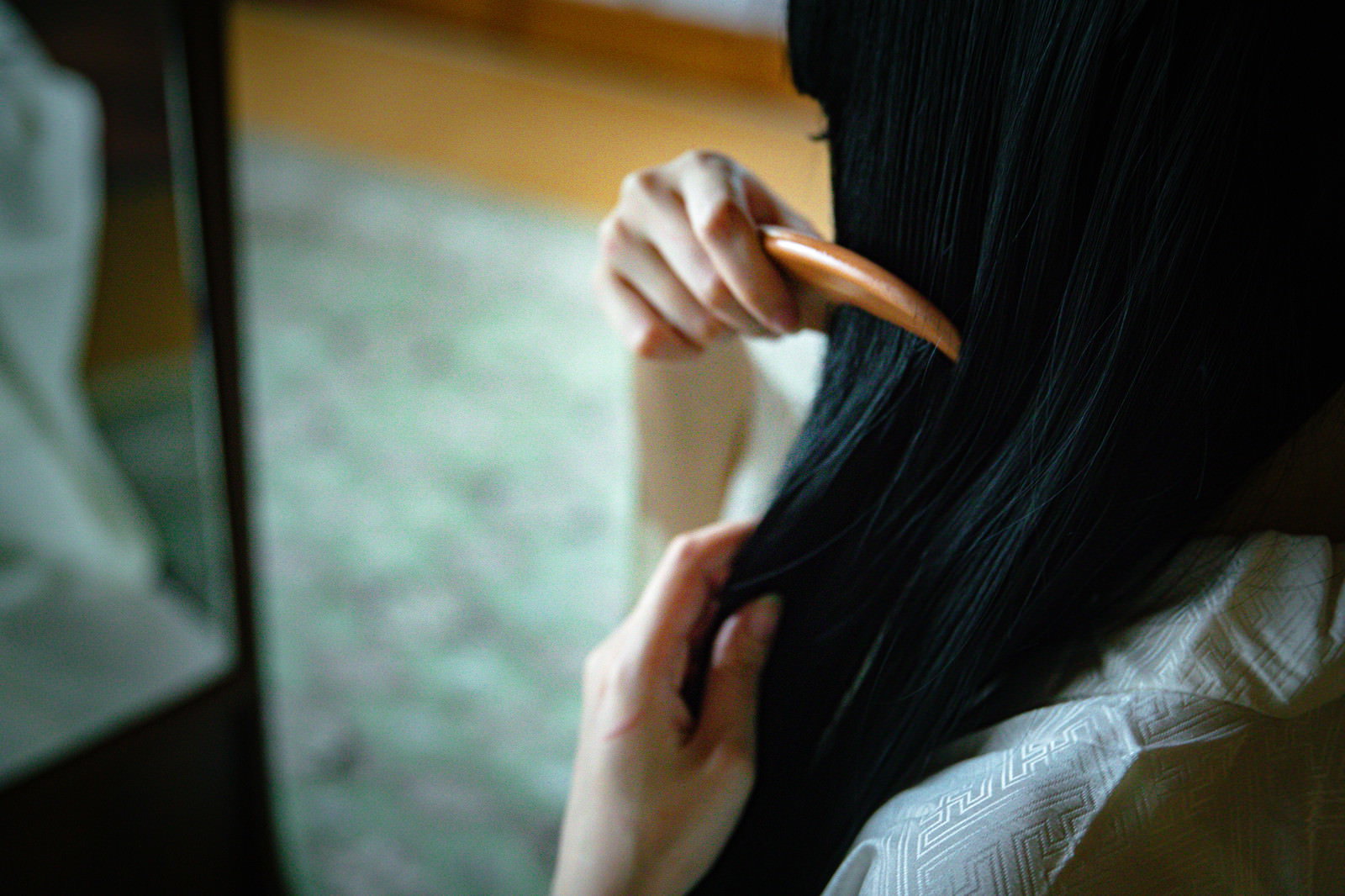 後ろ姿で座り黒髪に櫛をとおしている女性［モデル：緋真煉］