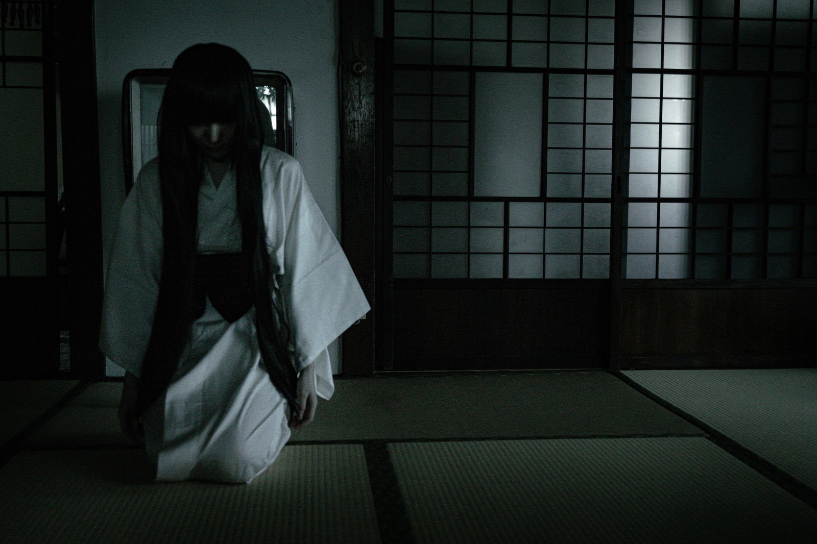 薄暗い畳の和室で白装束を着た髪の長い女性がうつむいている［モデル：緋真煉］