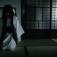 薄暗い畳の和室でうつむく髪の長い白装束の女性の写真
