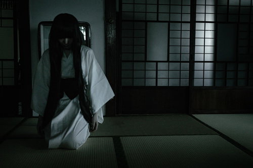 薄暗い畳の和室でうつむく髪の長い白装束の女性