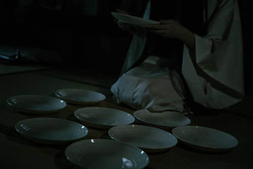 暗闇で皿を数える幽霊のような女性 - 皿屋敷の怪談表現